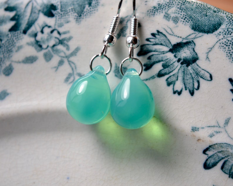 May include: A pair of silver teardrop earrings with light blue glass drops.