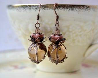 May include: Dangle earrings featuring round, translucent amber-colored glass beads encased in copper-toned metal leaf filigree caps, topped with small pink flower-shaped beads and copper-toned ear wires for pierced ears.