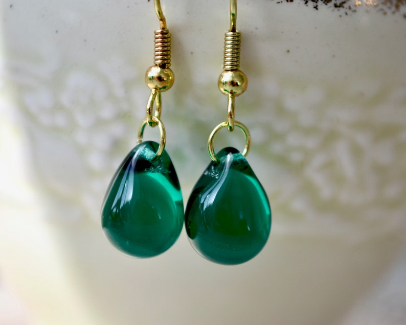 Glass teardrops in a lovely dark green are simply suspended from gold-plated earring hooks and displayed on the rim of a vintage teacup.