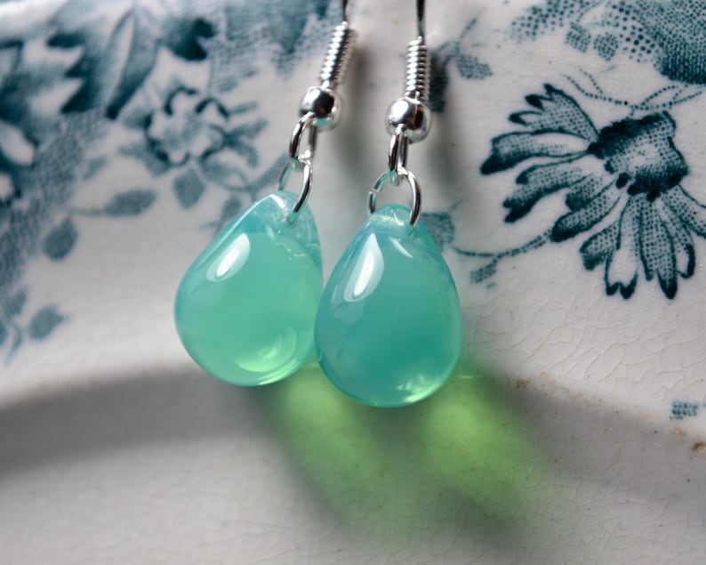 A pair of glass teardrop earrings with opalescent seafoam glass drops dangling from silver-plated hooks.