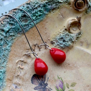 Glossy opaque cherry red glass teardrops are suspended from gunmetal silver-plated kidney hooks in these long dangle earrings.