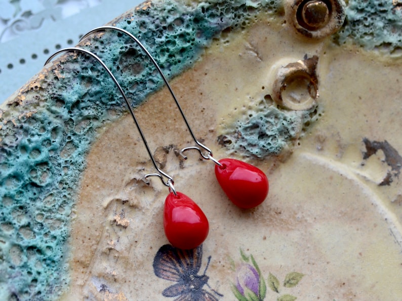 Glossy opaque cherry red glass teardrops are suspended from gunmetal silver-plated kidney hooks in these long dangle earrings.