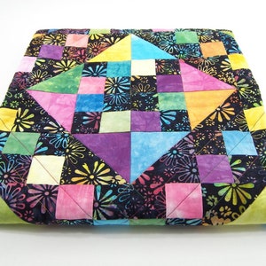 May include: A colorful patchwork quilt with a black background and a floral pattern. The quilt is made up of squares and triangles in various shades of pink, purple, blue, green, and yellow.