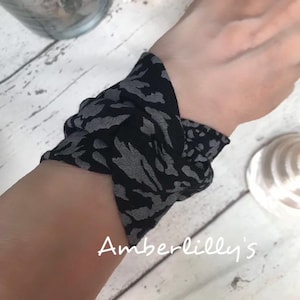 May include: A black and grey patterned fabric wristband. The fabric features a repeating animal print design. The wristband is knotted and wrapped around a wrist. The text "Amberlilly's" is written in cursive on the bottom of the image.