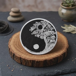 May include: A circular embroidered patch featuring a black and white yin yang design. The white section depicts a detailed tree with a circular sun, while the black section contains a smaller white circular moon. The patch has a white border.