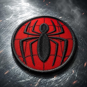 May include: A circular embroidered patch featuring a vibrant red background with a black spider emblem at the center. The design includes a thin black web pattern stitched over the red surface, finished with a thick black stitched border edge.