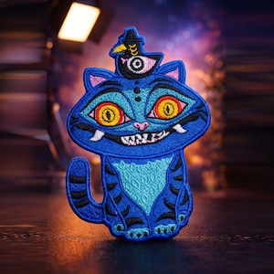 Puede incluir: Un parche bordado que muestra un gato azul con una amplia sonrisa, grandes ojos amarillos y un pecho azul claro con patrones. Un pequeño pájaro negro con un ojo blanco se posa sobre la cabeza del gato, usando hilos de colores azul, amarillo y negro.