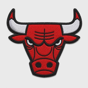 Puede incluir: Un parche bordado con el logotipo de los Chicago Bulls, una cabeza de toro estilizada en hilo rojo, blanco y negro. El diseño muestra cuernos angulares afilados, ojos intensos y un contorno marcado, creando un gráfico texturizado de alto contraste.