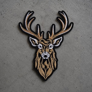 May include: An embroidered patch featuring the head of a deer with large antlers. The design uses gold, white, and black thread to create a detailed, stylized representation of the animal, with a black border outlining the entire shape.