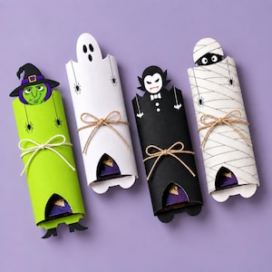 May include: Four cylindrical paper candy wrappers featuring Halloween characters: a green witch, a white ghost, a black vampire, and a white mummy. Each wrapper is tied with a brown twine bow and displays a small portion of a dark chocolate bar.