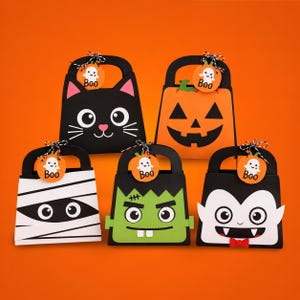 May include: Five Halloween-themed paper gift bags with handles, each featuring a round tag with a ghost and the text Boo. Designs include a black cat, an orange jack-o'-lantern, a white mummy, a green monster with stitches, and a vampire with a red bow tie.