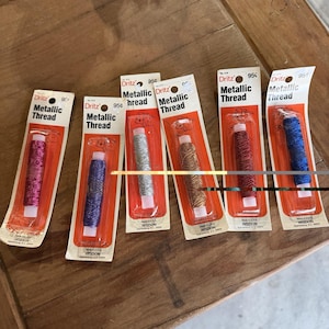 May include: Six individual packages of Dritz Metallic Thread, each featuring a different color spool: magenta, purple, silver, gold, red, and blue. Each card displays the brand name, the text Metallic Thread, and a price of 95 cents.