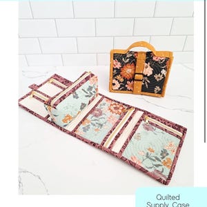 May include: A Nightingale Zipper Case quilted supply case pattern by Center Street Quilts. The image shows one case folded shut in black with orange floral patterns and one case unfolded, revealing light blue interior panels with floral prints.