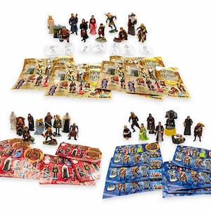 Puede incluir: Una colección de figuras en miniatura con temática de El Señor de los Anillos e insertos de papel. El conjunto incluye varios personajes en diversas poses, acompañados de múltiples folletos impresos con el texto Herr der Ringe.