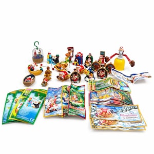 May include: A collection of small plastic Christmas-themed figurines, including Santa Claus figures, ornaments, and miniature scenes, accompanied by several colorful paper instruction leaflets featuring German text and illustrations of holiday characters.