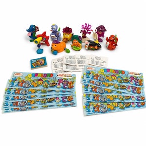 May include: A collection of ten colorful plastic Kinder Joy toy figurines featuring various aquatic creatures, accompanied by a small booklet, several white paper instruction cards, and multiple rectangular paper strips labeled Aqualand.