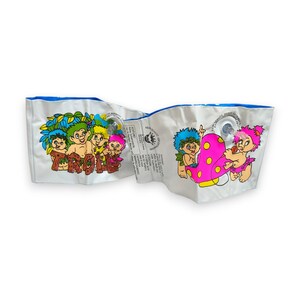 Puede incluir: Un par de flotadores de brazo inflables blancos con personajes de trolls de dibujos animados coloridos y la palabra TROLLS impresa. Cada flotador incluye una válvula de aire de plástico transparente y texto de seguridad impreso en negro.