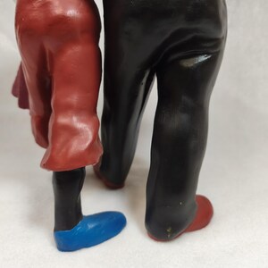 Op de afbeelding: Een beeldje dat de onderlichamen van twee figuren toont. E&eacute;n figuur draagt een rode broek en een blauwe schoen, terwijl de andere figuur een zwarte broek en een rode schoen draagt. De figuren staan naast elkaar met een gladde, geverfde afwerking.