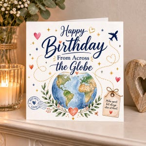 Könnte beinhalten: Eine quadratische Grußkarte mit dem Text Happy Birthday From Across the Globe in blauer Schrift. Das Design zeigt einen Aquarell-Globus, ein kleines Flugzeug, rote Herzen, goldene Sterne, einen Poststempel und ein Etikett mit der Aufschrift Miles apart, but always close at heart.