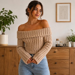 May include: A beige off-the-shoulder long-sleeve sweater featuring a thick ribbed knit texture and a wide folded collar. The garment is paired with light blue denim jeans, creating a casual look with a fitted silhouette and long sleeves.