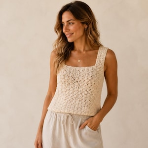 Op de afbeelding: Een mouwloze, crèmekleurige gehaakte tanktop met een vierkante halslijn en een ingewikkelde opengewerkte textuur, gecombineerd met een lichtbeige broek met trekkoord die een gladde, effen stofafwerking en een relaxte pasvorm heeft.
