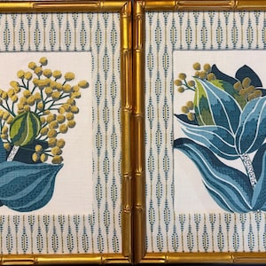 May include: Two rectangular framed wall art pieces featuring gold bamboo-style frames. Each print displays a white background with a blue and gold vertical dotted pattern, centered with a botanical illustration of blue leaves and yellow flowers.