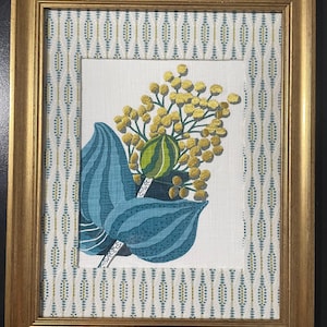 May include: A framed artwork featuring a central botanical illustration of yellow mimosa flowers and a green striped seed pod set against a white background. The image is bordered by a repeating geometric pattern of blue and gold vertical lines.