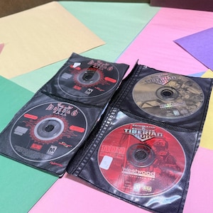 May include: Four circular PC game discs housed in a black plastic sleeve. Two discs are labeled Diablo II with black and red graphics. Two discs are labeled Command & Conquer Tiberian Sun, one with a gold and black design and one with red graphics.