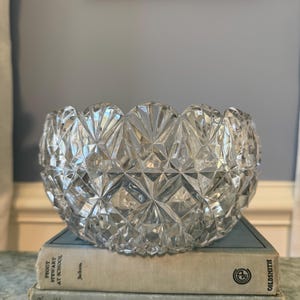 May include: A clear, faceted glass bowl with a scalloped rim and geometric diamond-cut patterns. The bowl rests on two stacked hardcover books titled Peggy Stewart at School by Jackson and Lavender and Old Lace by Reed, both published by Grosset & Dunlap.
