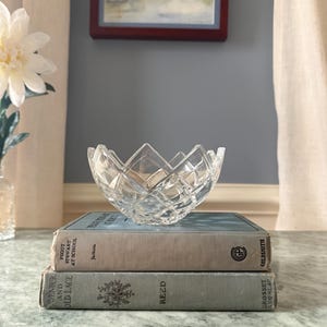 May include: A clear, cut-glass bowl with a diamond-patterned exterior and a jagged, pointed rim. The bowl is resting on top of two stacked hardcover books, with the top book titled Peggy Stewart at School and the bottom book titled Lavender and Old Lace.