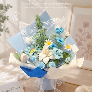 May include: A handmade crochet flower bouquet featuring various blue, white, and green yarn flowers, including daisies and lilies. The bouquet is wrapped in blue and white paper with lace trim and includes a card with the text Happy Flower.