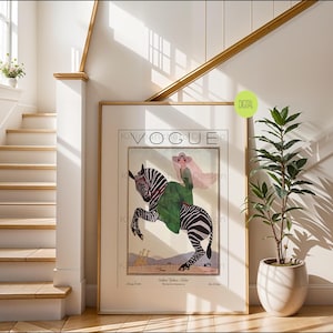 May include: A framed wall art print featuring a vintage-style Vogue magazine cover illustration. The artwork depicts a person in a green dress and wide-brimmed hat riding a zebra, with two giraffes in the background. The text reads Vogue.