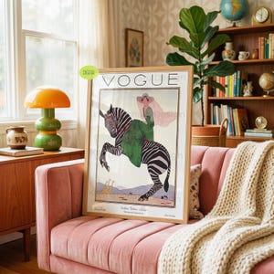 May include: A framed art print featuring a vintage Vogue magazine cover illustration. The image depicts a person in a green dress and wide-brimmed hat riding a zebra, with two giraffes in the background. The text reads VOGUE at the top.