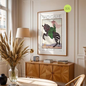 May include: A framed wall art print featuring a vintage Vogue magazine cover illustration. The artwork depicts a person in a green coat and pink hat riding a zebra, with two giraffes in the background. The text VOGUE is printed at the top.