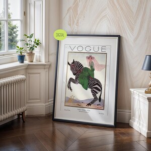 May include: A framed wall art print featuring a vintage Vogue magazine cover illustration. The artwork depicts a person in a green coat and wide-brimmed hat riding a zebra. The background shows a desert landscape with small giraffes in the distance.