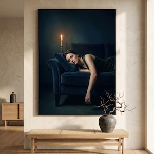 May include: A large framed wall art print depicting a person in a dark green dress reclining on a deep blue velvet sofa. A single lit candle in a brass holder sits on the sofa back. The scene is set against a dark, moody background.