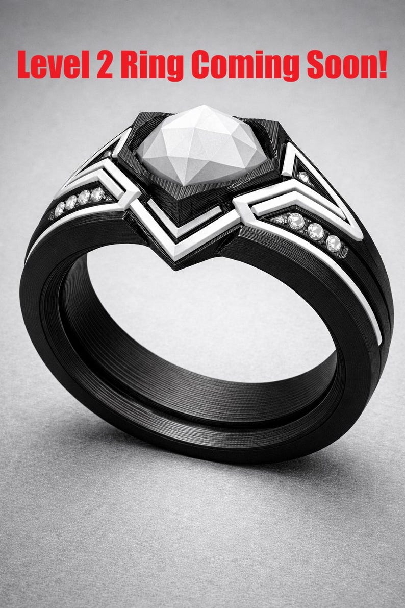 May include: A black ring with a faceted white centre stone and white geometric accents along the band, featuring small embedded clear stones. The text Level 2 Ring Coming Soon! is displayed in red at the top of the image.
