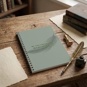 May include: A sage green spiral-bound notebook featuring a feather illustration and the text "MY LIFE LIST IS LONG, BUT MY PATIENCE IS SHORT" printed on the cover. The notebook is positioned alongside a gold wax seal stamp and a quill pen.