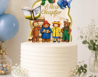 Könnte beinhalten: Ein weiß glasierter Kuchen mit einem dekorativen Aufsatz, der den Text A New Chapter, eine grüne Raupe, einen blauen Fisch, ein offenes Buch sowie Illustrationen von Curious George, Paddington, Madeline und einem Bären vor Büchern zeigt.