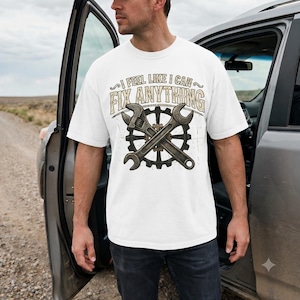 May include: A white short-sleeved t-shirt featuring a graphic print of two crossed metal wrenches over a black gear icon. The text "I FEEL LIKE I CAN FIX ANYTHING" is printed in a distressed, tan-colored font above the tools.