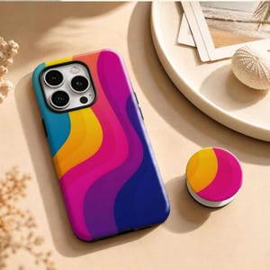 Puede incluir: Una funda para smartphone y un soporte circular a juego con un patrón ondulado vibrante de rayas en color verde azulado, amarillo, magenta y azul oscuro. La funda tiene una abertura para un sistema de cámara de tres lentes.