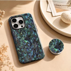 May include: A smartphone case and a matching circular phone grip featuring an iridescent abalone shell pattern with deep blue, green, and purple tones. The case has a cutout for a triple-lens camera system and a black border around the lenses.