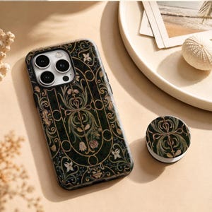 May include: A dark green smartphone case and a matching circular phone grip featuring an intricate pattern of gold-toned lines, stylised floral motifs, and delicate botanical elements in shades of cream, pink, and muted green throughout the design.