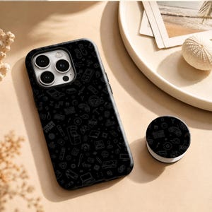 May include: A black smartphone case and a matching circular phone grip, both featuring a repeating pattern of thin white line art icons related to video games, including controllers, consoles, and the text "GAME OVER" and "PRESS START".