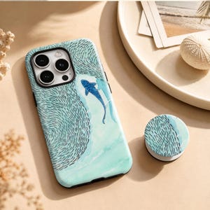 Peut inclure: Une coque de smartphone bleu clair et un support de téléphone circulaire assorti présentant une illustration style aquarelle d'un banc de petits poissons nageant en tourbillon autour d'un grand requin bleu dans une eau turquoise.