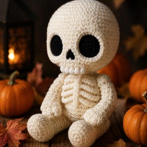 May include: A crocheted skeleton doll made of off-white yarn with large, circular black eye sockets, a small triangular nose, and a row of individual white teeth. The figure has a rounded head, a ribcage design, and sits in a seated position.