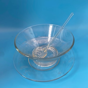 May include: A clear glass bowl and matching saucer set featuring a delicate etched leaf pattern along the rims. A clear glass ladle with a shell-shaped bowl and a long, slender handle rests inside the bowl, completing this elegant serving set.