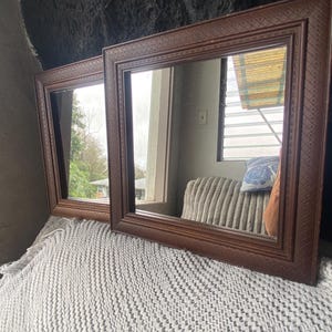 May include: Two square mirrors with dark brown wooden frames featuring a textured, cross-hatched pattern along the edges. The frames have a multi-layered, stepped profile design that adds depth to the overall appearance of the mirrors.