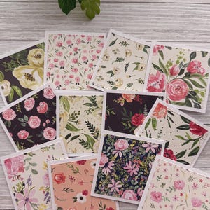 May include: A collection of square floral cards with white borders. The cards feature various floral patterns, including roses, peonies, and other blooms in shades of pink, yellow, and purple. The cards are arranged on a light wood-grain surface.