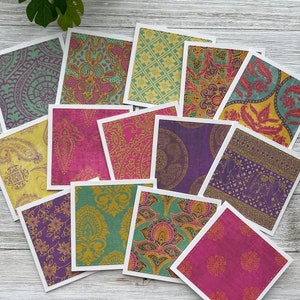 May include: A set of 14 square cards with different patterned designs. The patterns are in shades of purple, pink, yellow, and green. The cards are arranged in a circle on a white wooden surface.